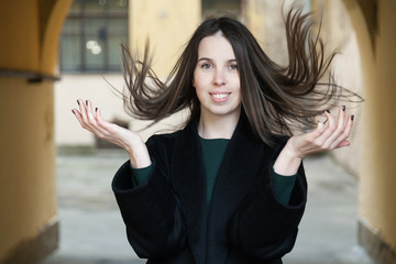 A long-haired girl in a black coat and a green dress walks through the shabby courtyards of the old...