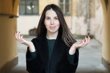 A long-haired girl in a black coat and a green dress walks through the shabby courtyards of the old...