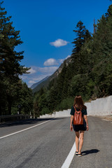 An active healthy female hipster model walking along a forest mountain road. Rear view