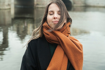 Stylish long-haired girl in a black coat with a red scarf smiles on the embankment of the Fontanka River