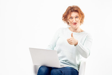 Portrait of a red haired mature woman with content or satisfied expression on her face with a laptop and thump up against white background