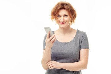 Portrait of a smiling red haired mature woman with a phone in her hand against white background. Happy mother communicating with family via mobile phone