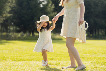 Hispanic girl holding her mother's hand in the park at sunset - Girl smiling watching the camera...