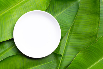 Empty white ceramic plate on banana leaves background. Top view