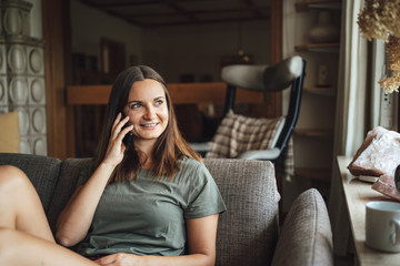 Obraz premium Young Caucasian woman looking away while talking on mobile phone, sitting on sofa at home