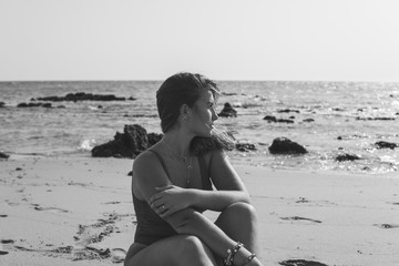 Grayscale shot of a beautiful European female with a swimsuit sitting on the beach