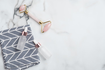 Face massage tool and serum dropper bottles on white marble desk. Anti aging, lifting, facial skin treatment concept. Flat lay, top view.