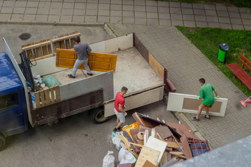 Workers load old furniture into the back of a truck to transport