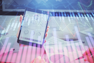 Double exposure of man's hands holding and using a digital device and forex graph drawing. Financial market concept.