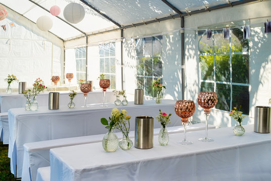 Wedding table setting decorated with fresh flowers in a vase, champagne coolers, and decorative glasses. Banquet table for guests outdoors with a view of green nature.