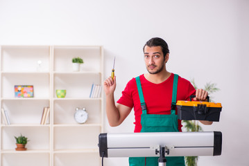Young male contractor repairing heater indoors