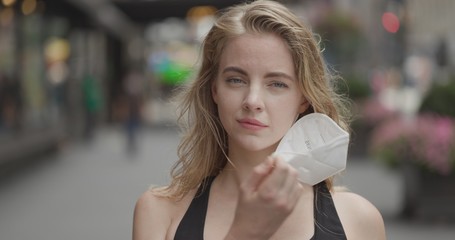 Young blond woman in city face portrait taking off a mask