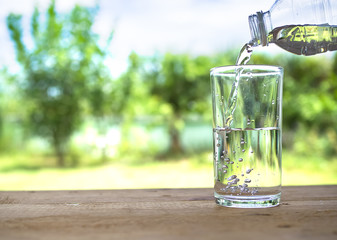 Pouring pure water into a glass on wood with blur image of leave green. Healthy lifestyle and ideal for environmental protection concept.