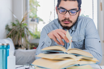 Concentrated student turning pages of a textbook, next to other open books on the desk, studying...