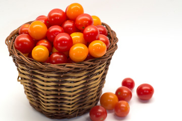 Up close picture of many cherry tomatoes in a brown wicker basket isolated against white background