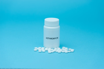 AZITROMYCIN antibiotic in white bottle packaging with scattered pills. Treatments for COVID-19. isolated on blue background. Copy space. Horizontal shot.