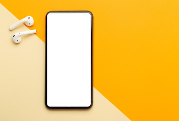 Flat lay, top view of orange office table desk with smartphone blank screen mockup with clipping path and wireless earphones. Modern working space.