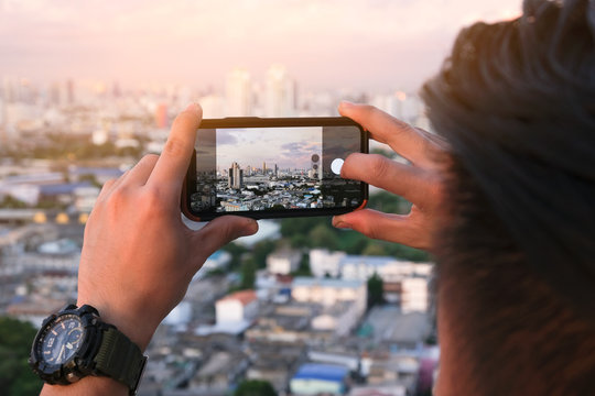 Young man take pictures of the buildings in the city. Sunrise time He uses a high-angle recording photo phone. concepts  technology