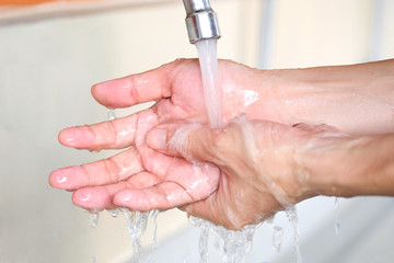 Hands of woman wash their hands in a sink with foam to wash the skin and water flows through the hands. Concept of health, cleaning and preventing germs and coronavirus from contacting hands