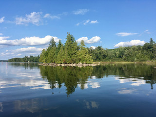 Trees reflected in the water at McGrath Pond, a pretty lake in Maine on a sunny day with clouds