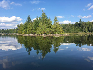 Fototapeta premium Trees reflected in the water at McGrath Pond, a pretty lake in Maine on a sunny day with clouds
