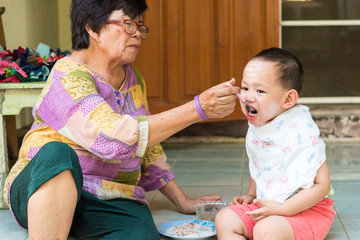 Grand mother feeding food to Thai baby boy