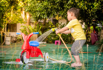 Asian boy washing red bicycle by green water sprayer
