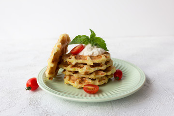 Zucchini waffles in a stack on a green plate served with sour cream, decorated with basil.