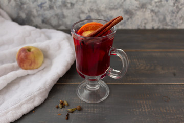 Mulled wine in a glass mug with cinnamon on a wooden table, next to an apple on a blanket.