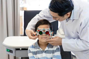 An Asian optometrist examines a child's eyesight using a Trial Frame. The boy patient visits an ophthalmology clinic.