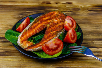 Grilled salmon steak with spinach and tomatoes on wooden table
