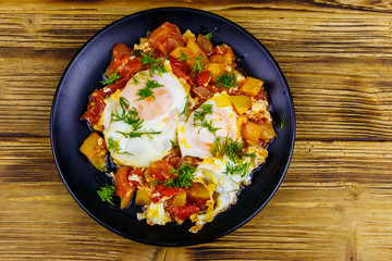 Homemade breakfast shakshuka - fried eggs, onion, bell pepper, tomatoes and dill on rustic wooden table. Jewish cuisine. Top view