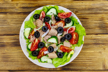 Tasty tuna salad with lettuce, black olives and fresh vegetables on wooden table. Top view