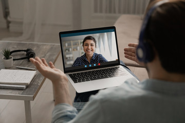 Fototapeta na wymiar Over shoulder view of man speak talk on video call on laptop with smiling ethnic woman wife, male have webcam virtual digital conference or online business meeting with colleague at home office
