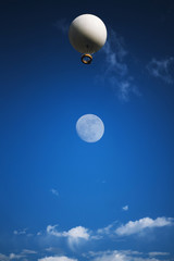 Air excursion balloon with a basket for passengers against the background of a bright blue sky with white clouds.