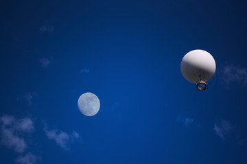 Air excursion balloon with a basket for passengers against the background of a bright blue sky with white clouds.
