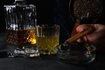 Glass of the whiskey with ice cubes and a square decanter, and cigar on a black  background.