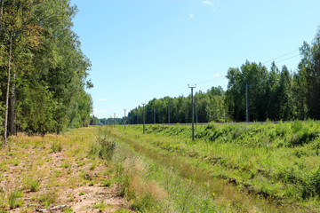 railroad tracks in the countryside surrounded by forest under bright blue summer sky