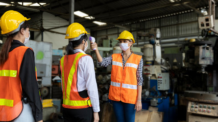 Factory in new normal. Worker uses infrared thermometer measuring temperature with  staff scanning for Coronavirus or Covid-19 symptom at factory entrance. International medical healthcare system