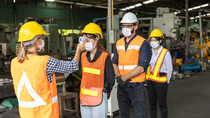 Factory in new normal. Worker uses infrared thermometer measuring temperature with  staff scanning...