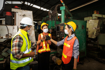Factory in new normal. Foreman wearing face mask giving explanation to new trainees in a factory warehouse. Male supervisor giving instruction to his co-workers