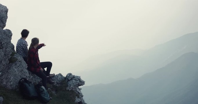 Friends hiking sit rest together on the rock at the top of peak summit view in the evening light smile have fun enjoy look at cloudy valley on an autumn or fall hike silhouette slow motion