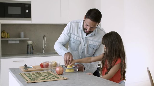 Young dad and daughter enjoying cooking together, squeezing lemon juice at kitchen counter. Medium shot, copy space. Family cooking concept