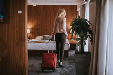 Young businesswoman arrives in a hotel room with red suitcase