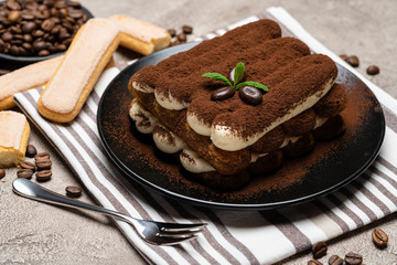 Classic tiramisu dessert and savoiardi cookies on ceramic plate on concrete background