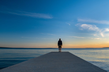 Man standing on long dock and watching sea horizon in sunset, island od Pag, Adriatic sea, Croatia,...