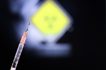 Medical syringe with a needle and a cure for the virus. A drop of drug flows down the needle....