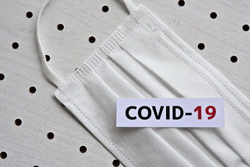 A disposable mask and a piece of paper printed with the letters "COVID-19" of the coronavirus.