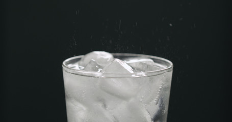 soda in glass with ice cubes on black background closeup
