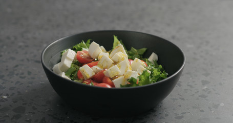 add olive oil to salad with mozzarella, cherry tomatoes and frisee leaves in black bowl on terrazzo surface